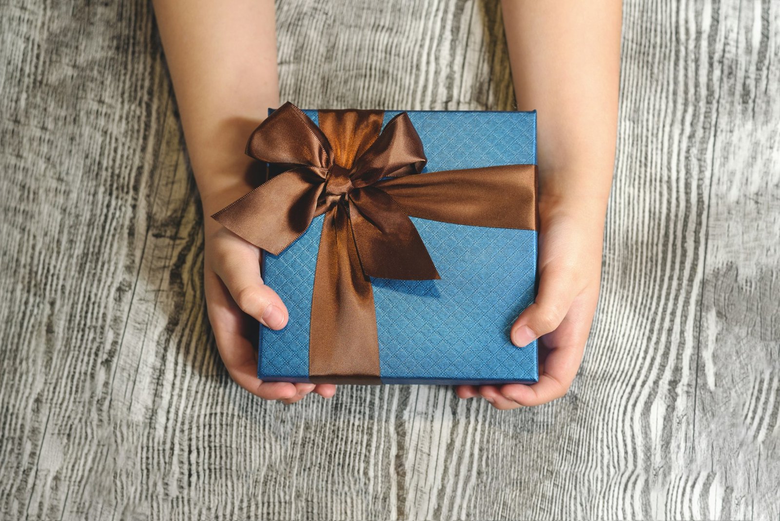 Kids hands holding a gift on the wooden background.